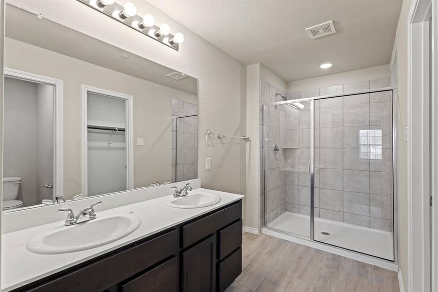 Full bath with double vanity, light wood-style flooring, a walk in closet, and a shower stall Full bath with double vanity, light wood-style flooring, a walk in closet, and a shower stall