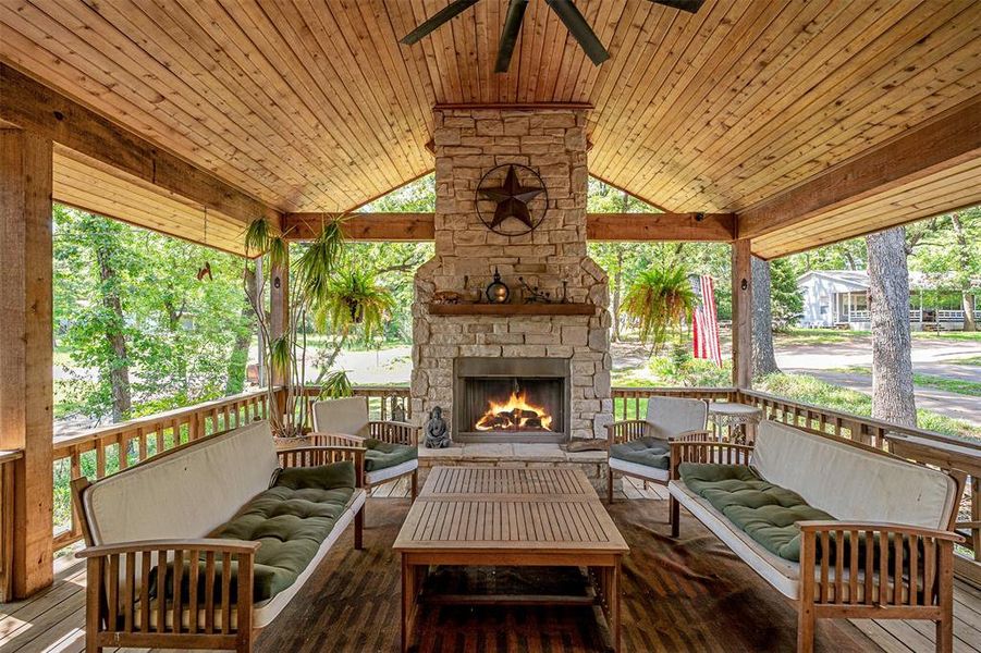 Expansive covered patio featuring a stone-clad fireplace, wood-planked ceiling, and wood-finish flooring