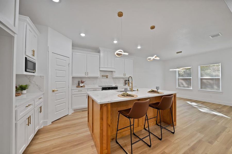 Kitchen featuring hanging light fixtures, a breakfast bar, white cabinets, light wood-style floors, and recessed lighting