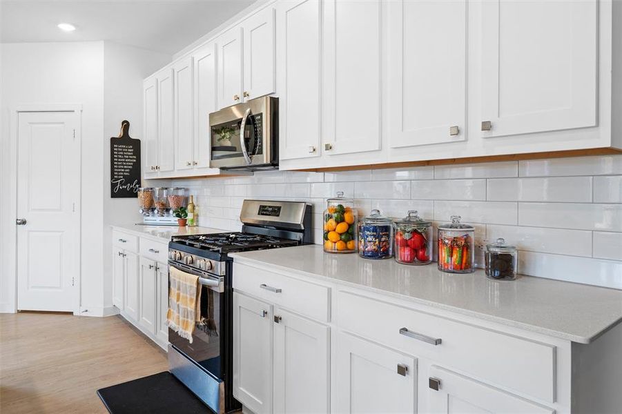 Kitchen featuring stainless steel appliances, white cabinets, decorative backsplash, light wood-style flooring, and light stone counters Kitchen featuring stainless steel appliances, white cabinets, decorative backsplash, light wood-style flooring, and light stone counters
