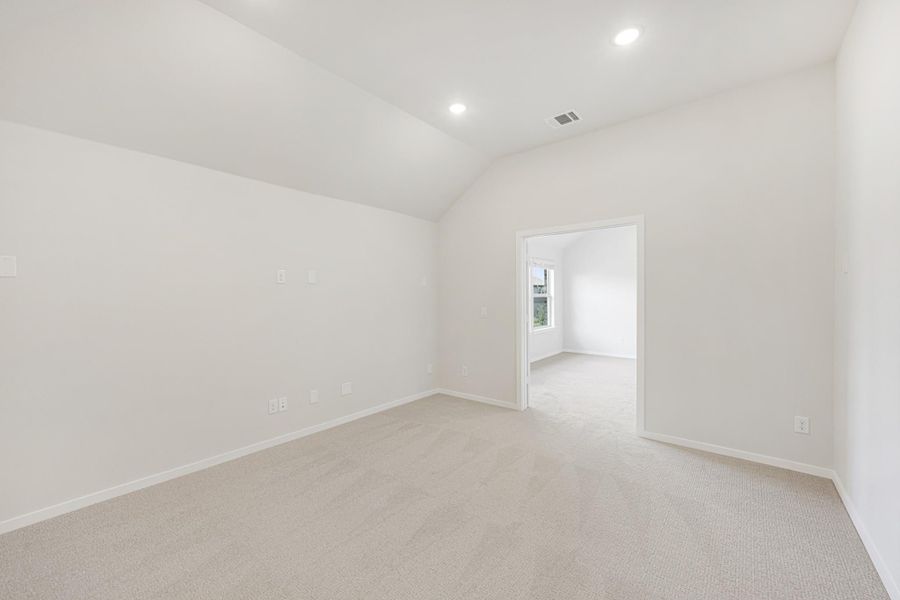 Empty bedroom with vaulted ceiling, white walls, carpet flooring, and open doorway to adjoining room