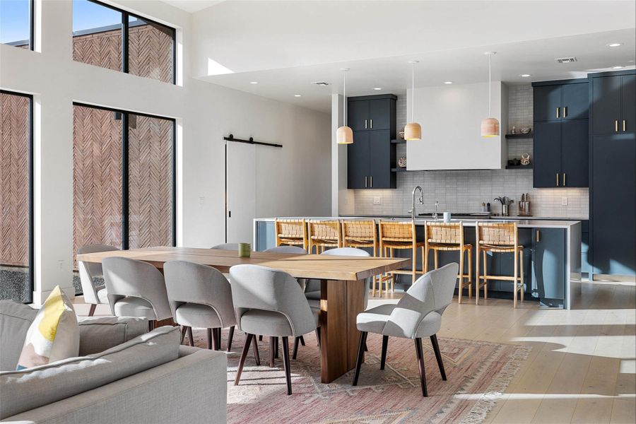 Dining area with a barn door, light wood-style flooring, a high ceiling, and recessed lighting