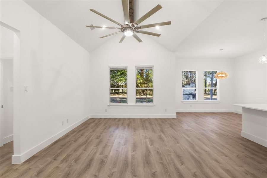 Unfurnished living room with plenty of natural light, high vaulted ceiling, ceiling fan with notable chandelier, and hardwood / wood-style flooring