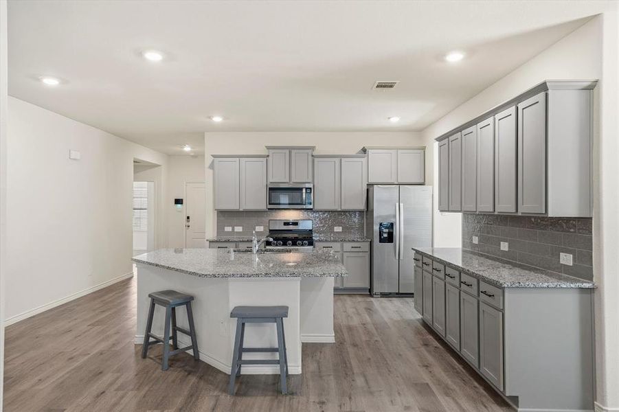 Kitchen with gray cabinets, stainless steel appliances, light stone countertops, a breakfast bar, and an island with sink Kitchen with gray cabinets, stainless steel appliances, light stone countertops, a breakfast bar, and an island with sink
