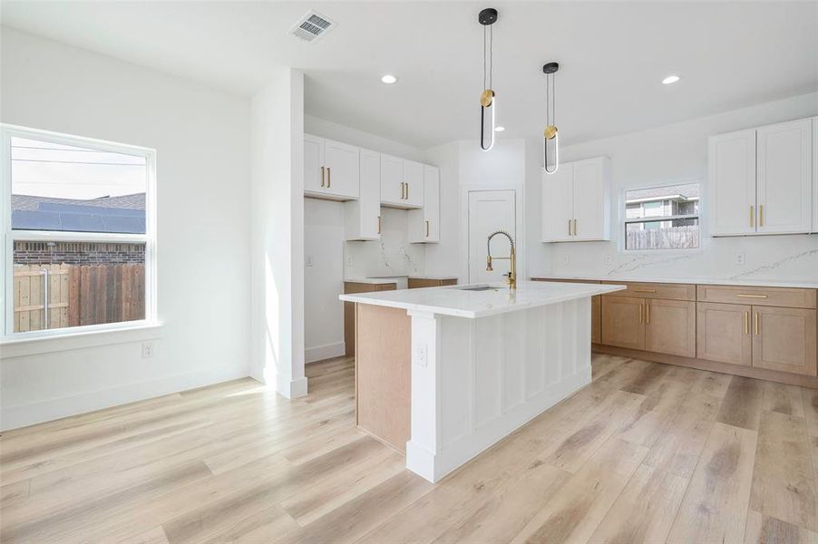 Kitchen featuring white cabinets, light wood-type flooring, a center island with sink, and plenty of natural light