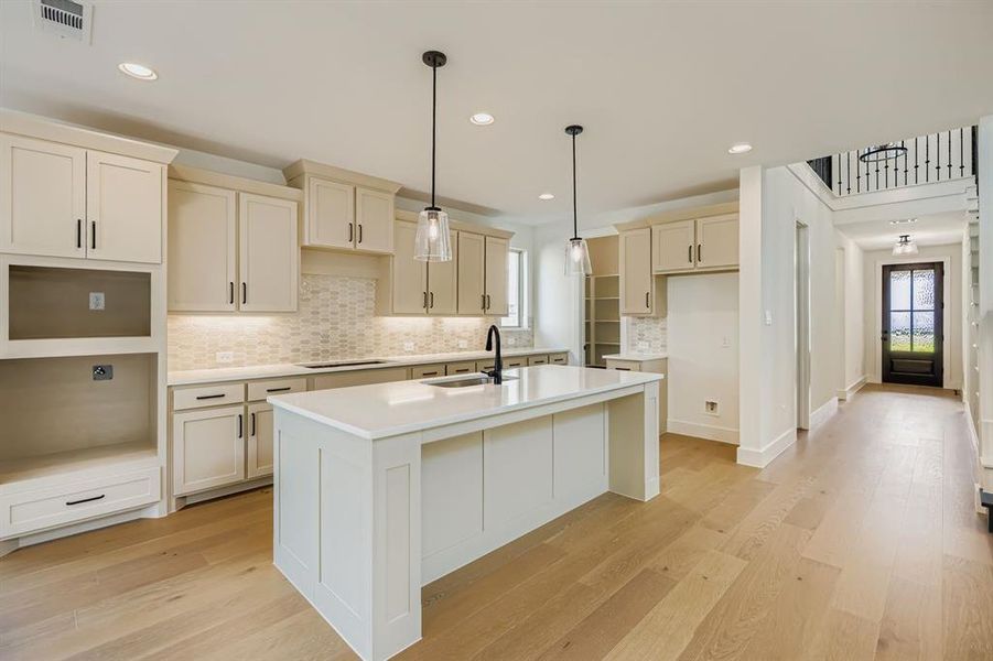 Kitchen with decorative backsplash, a kitchen island with sink, decorative light fixtures, light wood-style floors, and recessed lighting Kitchen with decorative backsplash, a kitchen island with sink, decorative light fixtures, light wood-style floors, and recessed lighting