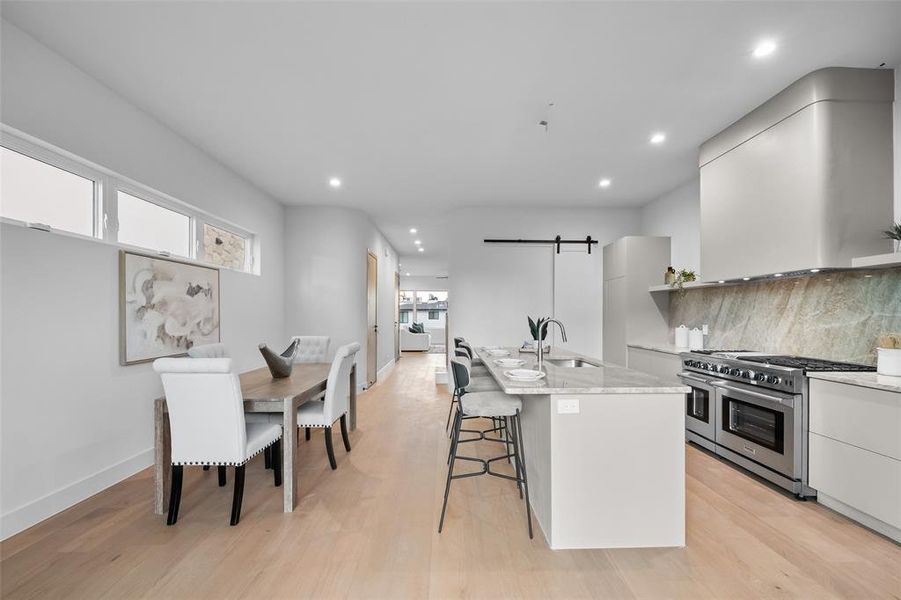 Kitchen with a barn door, modern cabinets, double oven range, light stone counters, and a kitchen island with sink