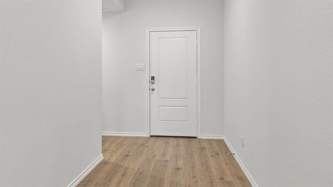 Hallway featuring wood-finish flooring, white baseboards, and a paneled door with a smart lock