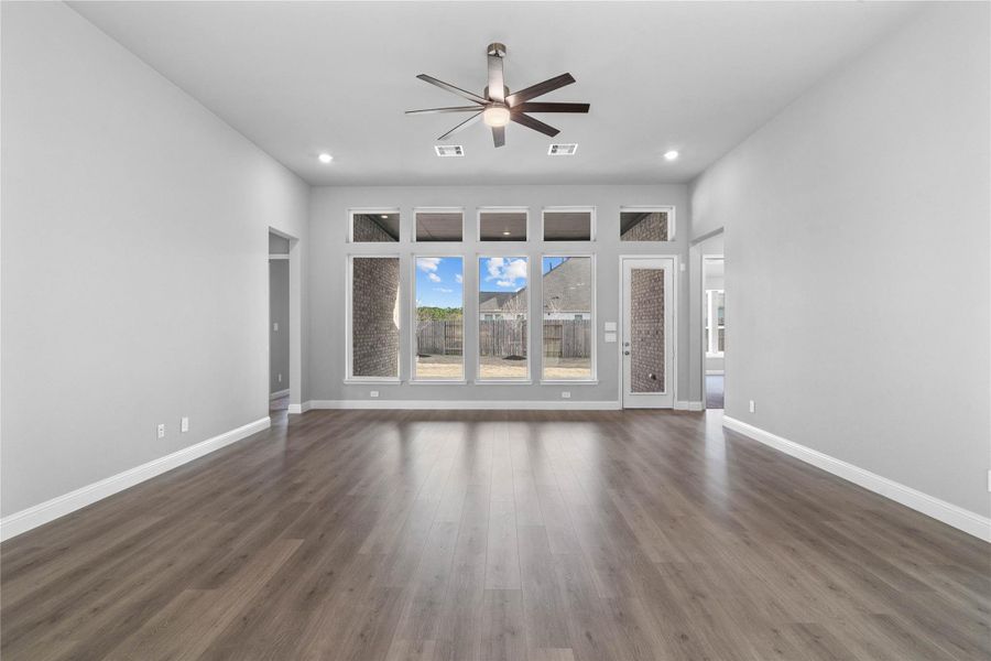 Enjoy the open and airy Family Room, designed for seamless entertaining and showcasing striking architectural details with high ceilings, recessed lighting, ceiling fan, durable laminate flooring, and a beautiful wall of windows that bring in an abundance of natural light and seamless flow to the covered rear patio.