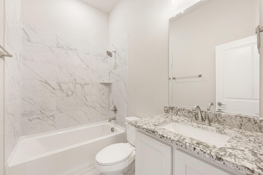 Bathroom with marble-look tile tub surround, granite vanity countertop, white cabinets, and large mirror