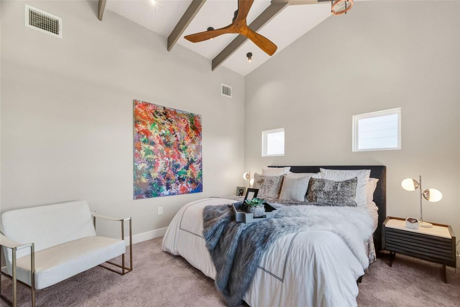 The primary suite occupies the top floor and impresses immediately with its vaulted ceiling featuring exposed decorative wood beams, large windows on two elevations, and plush carpet. A ceiling fan and generous square footage make this a true owner's retreat.