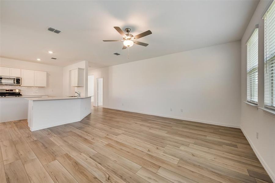 Unfurnished living room with sink, ceiling fan, and light wood-type flooring