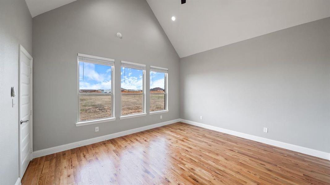 Empty room featuring high vaulted ceiling, recessed lighting, light wood-style flooring, and baseboards