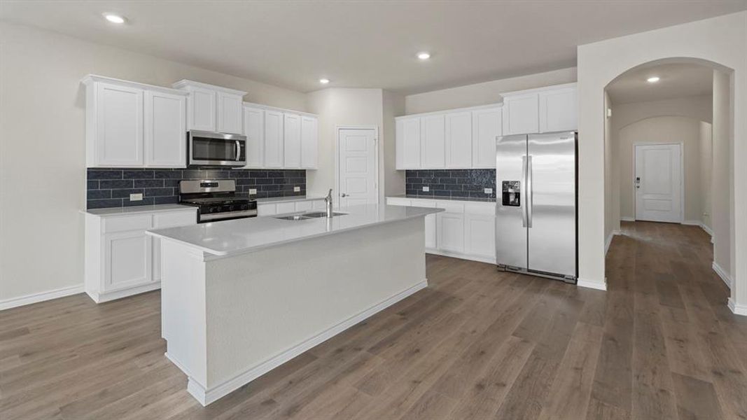 Modern kitchen featuring a central island with an undermount sink, white cabinetry, stainless steel appliances, and wood-finish flooring