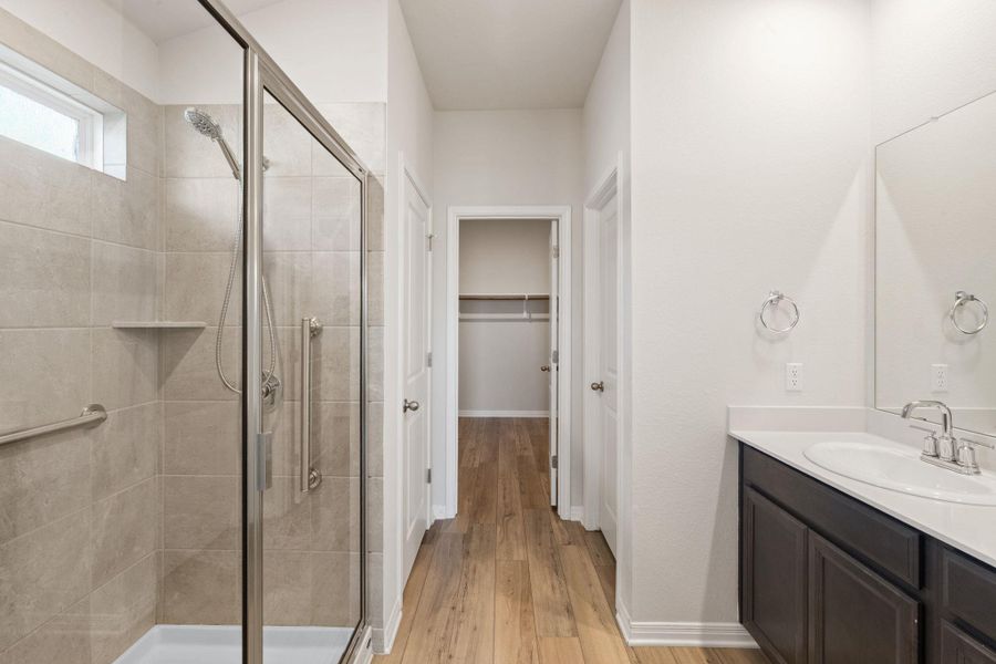 Full bathroom featuring vanity, a shower stall, a spacious closet, and light wood finished floors Full bathroom featuring vanity, a shower stall, a spacious closet, and light wood finished floors