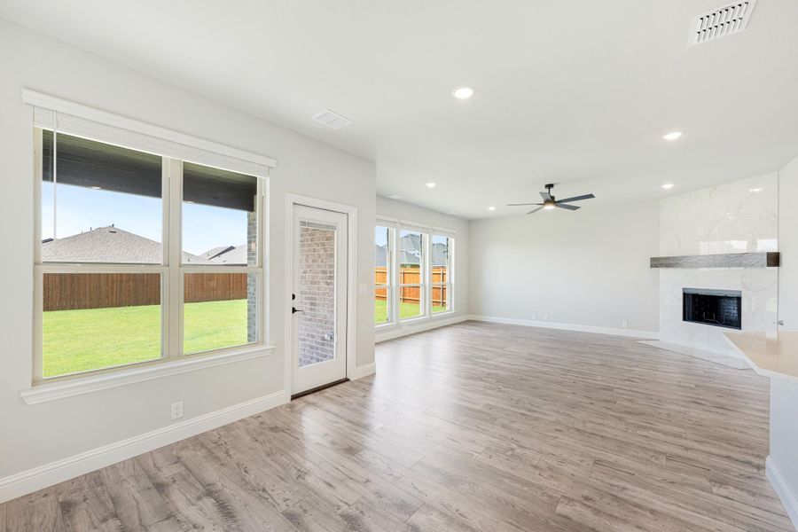 Open living room with light wood floors, fireplace, ceiling fan, and backyard windows