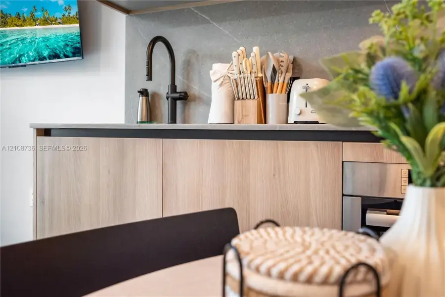 Kitchen area featuring flat-panel wood-finish cabinetry, a matte black high-arc faucet, and a stone-finish backsplash with integrated countertop Kitchen area featuring flat-panel wood-finish cabinetry, a matte black high-arc faucet, and a stone-finish backsplash with integrated countertop