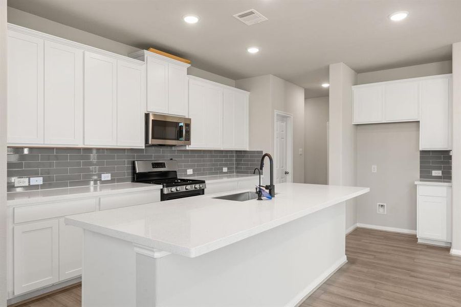 This light and bright kitchen features a large quartz island, white cabinets, a large sink overlooking your family room, recessed lighting, and beautiful backsplash.