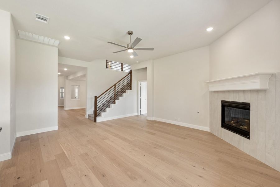 Open living room with light hardwood floors, ceiling fan, tile fireplace, and staircase with metal railing Open living room with light hardwood floors, ceiling fan, tile fireplace, and staircase with metal railing