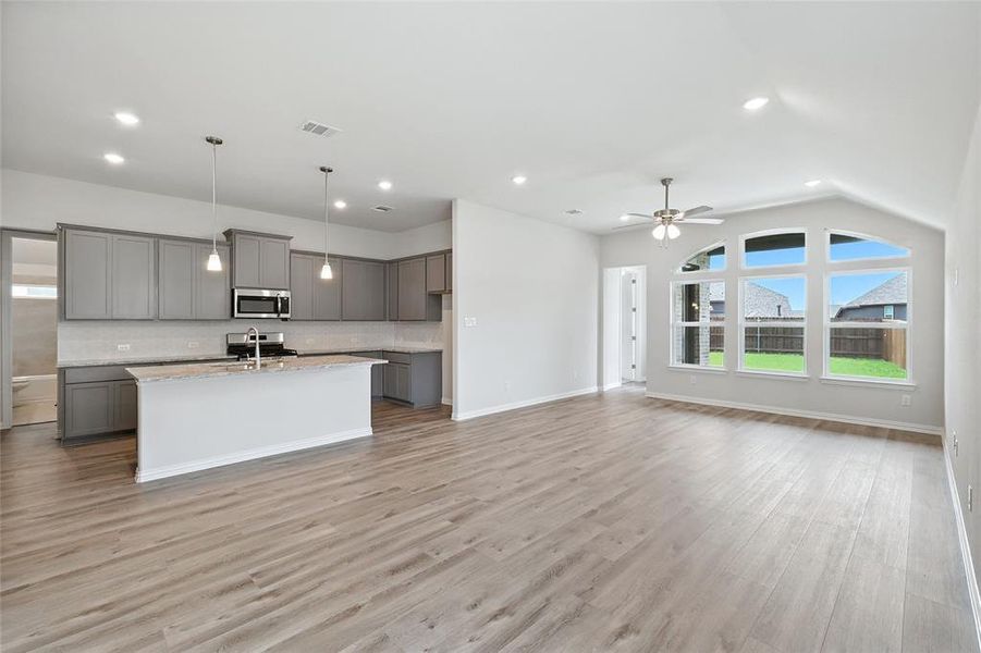 Kitchen with gray cabinets, open floor plan, backsplash, a center island with sink, and hanging light fixtures