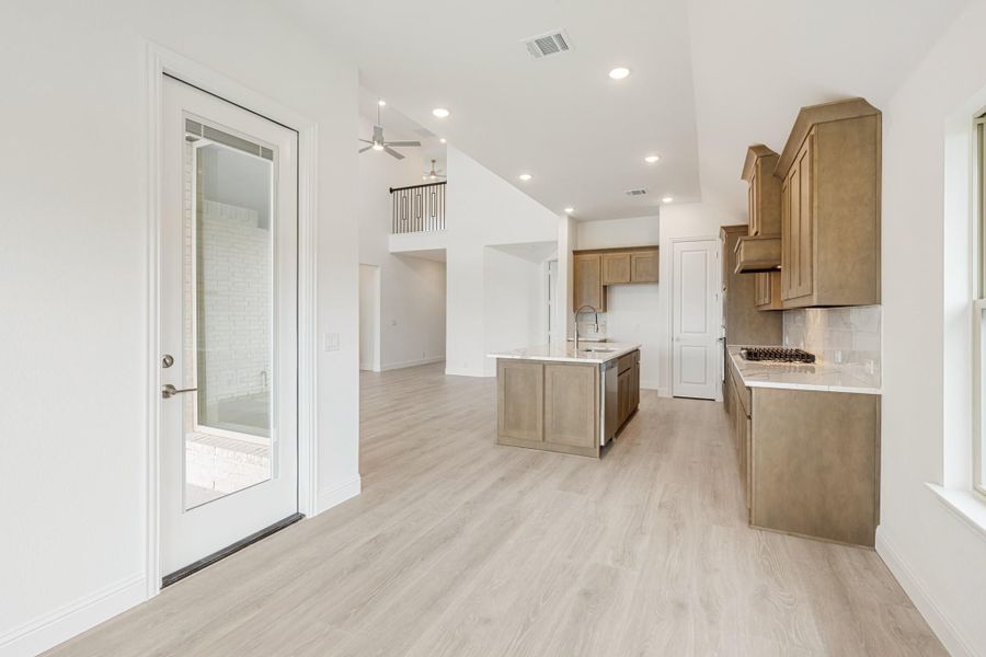 Open kitchen with tan wood cabinets, center island, light wood floors, and glass door to patio Open kitchen with tan wood cabinets, center island, light wood floors, and glass door to patio