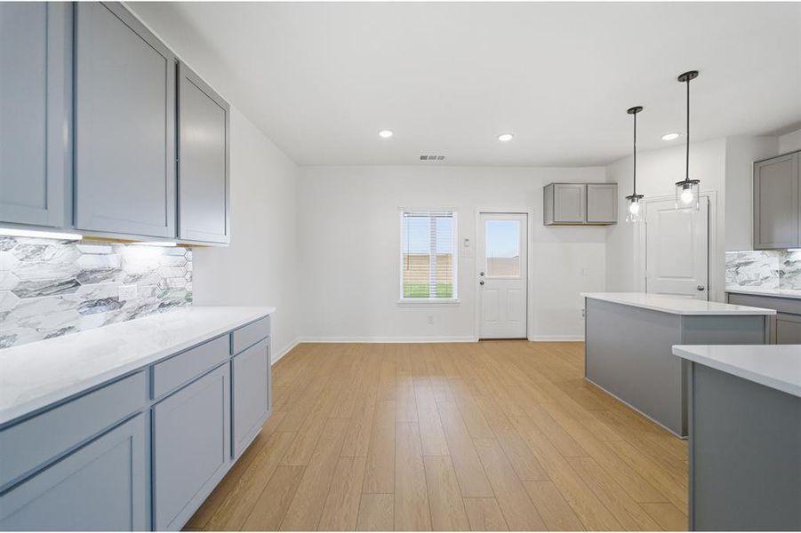 Kitchen featuring backsplash, gray cabinets, decorative light fixtures, light wood finished floors, and light stone countertops