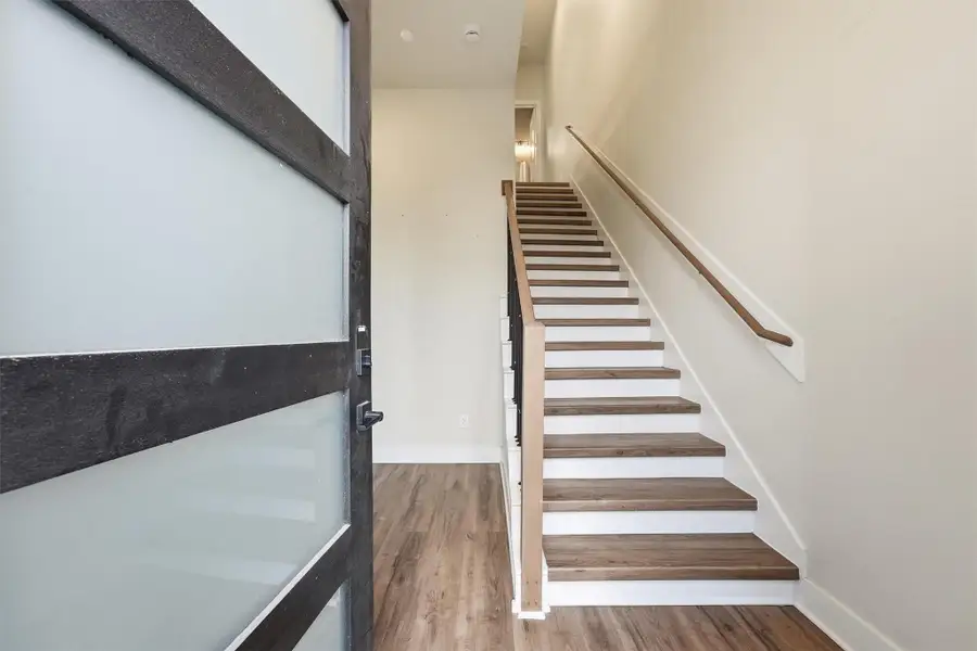 Bright entryway featuring modern wood-look flooring, a sleek glass-paneled door, and a staircase with clean lines leading to the upper living areas.