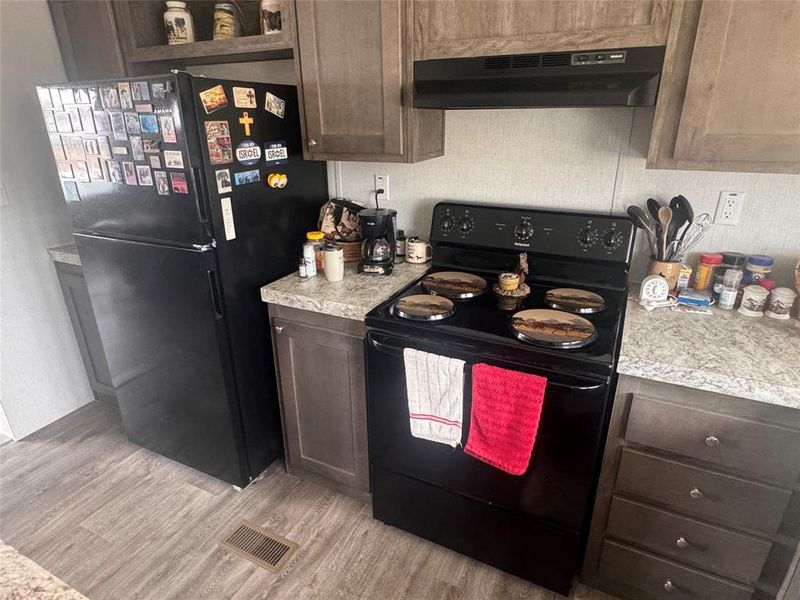 Kitchen featuring black appliances, light countertops, dark wood finish cabinets, and light wood-type flooring Kitchen featuring black appliances, light countertops, dark wood finish cabinets, and light wood-type flooring