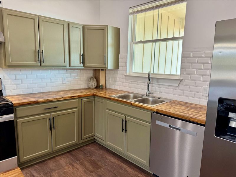 Kitchen featuring butcher block countertops, appliances with stainless steel finishes, dark wood-style flooring, and tasteful backsplash Kitchen featuring butcher block countertops, appliances with stainless steel finishes, dark wood-style flooring, and tasteful backsplash