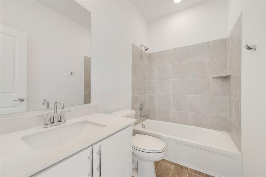 Full bathroom with hardwood / wood-style floors, vanity, tiled shower / bath combo, and toilet