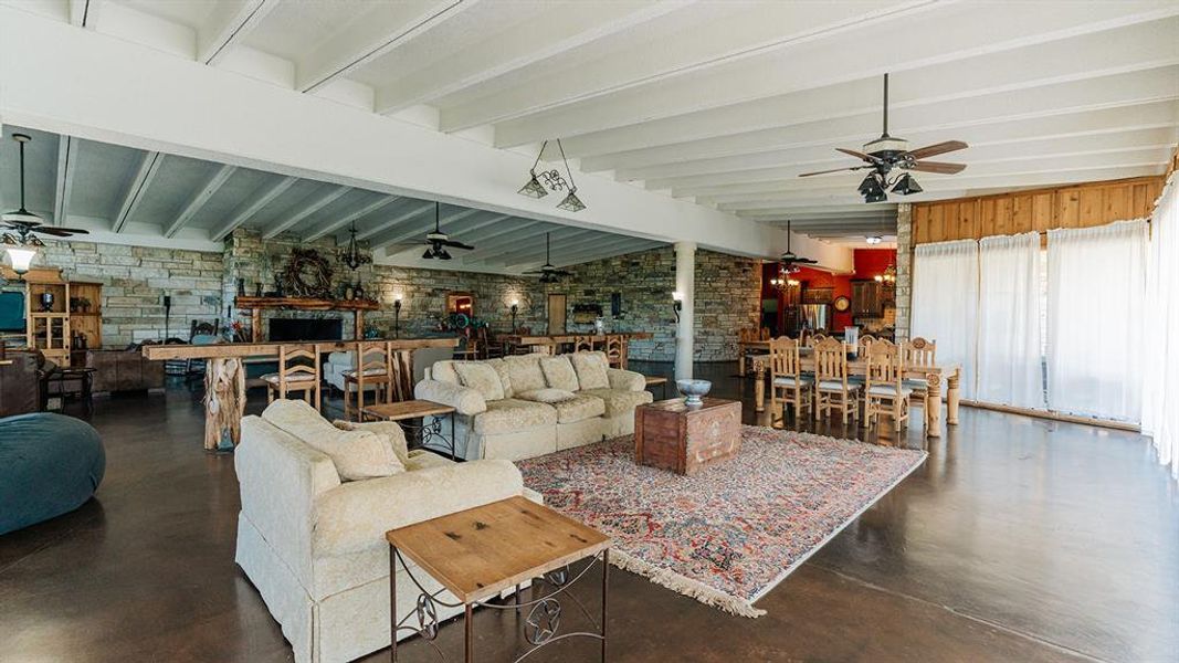 Living area featuring a ceiling fan, concrete floors, beamed ceiling, a fireplace, and brick wall