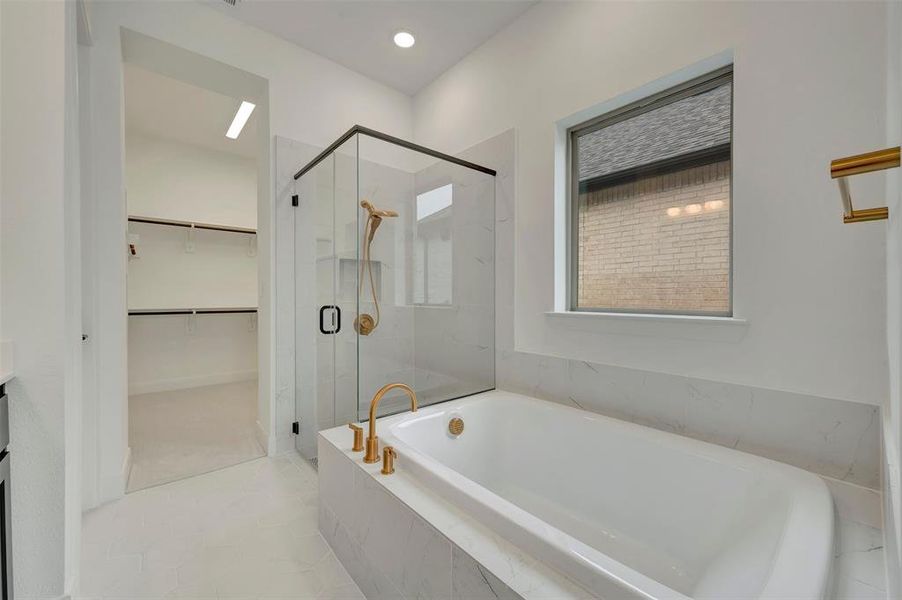 Bathroom featuring a freestanding soaking tub with brass fixtures, a glass-enclosed shower with black trim, and a window