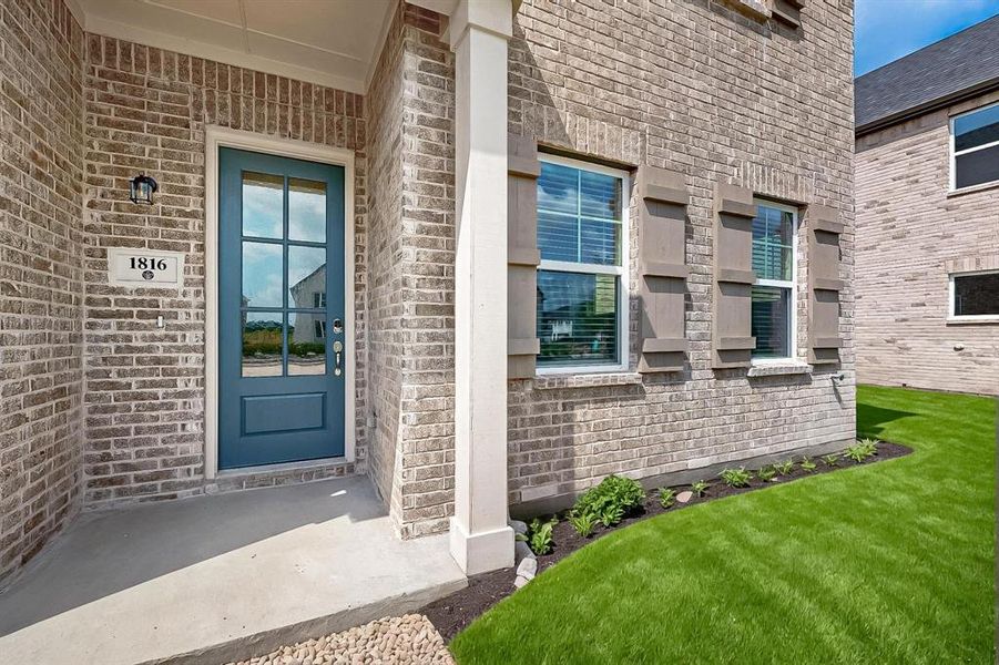 View of exterior entry with brick siding, a porch, and a yard