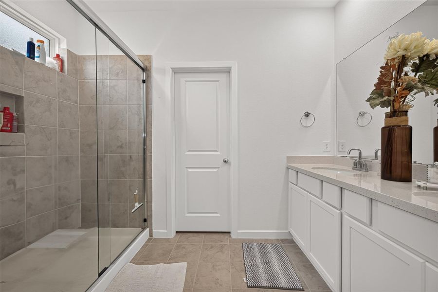 This bathroom is super spacious and features a big tiled shower with glass doors, a double vanity with sleek countertops, and really nice fixtures for a modern, high-end feel.