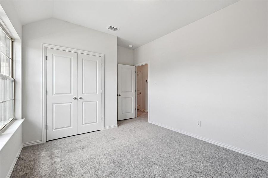 Unfurnished bedroom with light carpet, a closet, and lofted ceiling