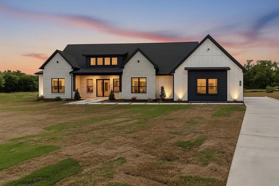 Modern inspired farmhouse featuring board and batten siding, a porch, a yard, brick siding, and roof with shingles Modern inspired farmhouse featuring board and batten siding, a porch, a yard, brick siding, and roof with shingles