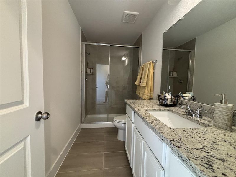 Bathroom featuring toilet, tile patterned floors, an enclosed shower, and vanity