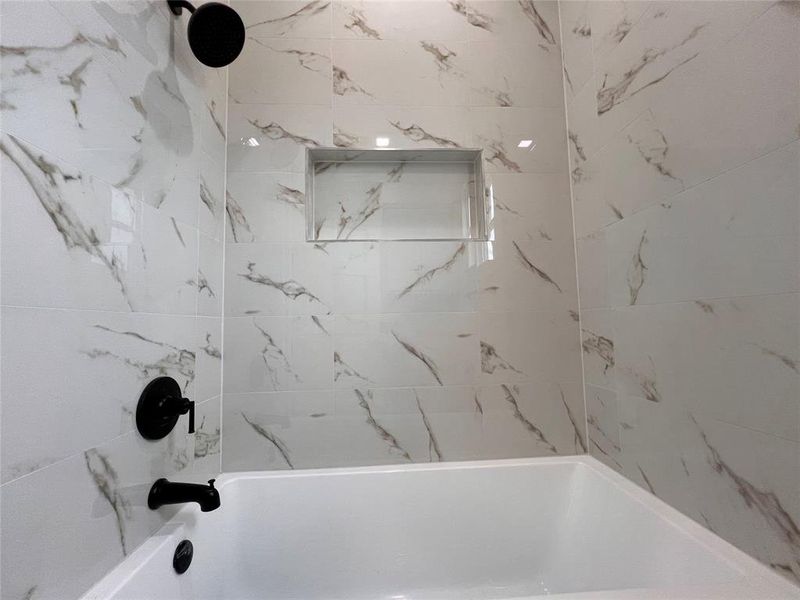 Bathtub with matte black fixtures, white tile surround with gray veining, and a recessed shower niche