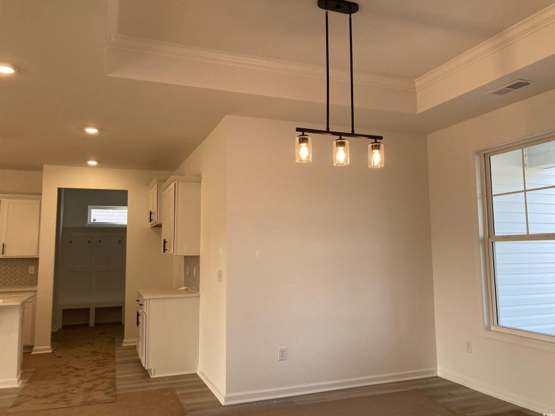 Unfurnished dining area with dark wood-style floors, ornamental molding, a tray ceiling, and recessed lighting Unfurnished dining area with dark wood-style floors, ornamental molding, a tray ceiling, and recessed lighting