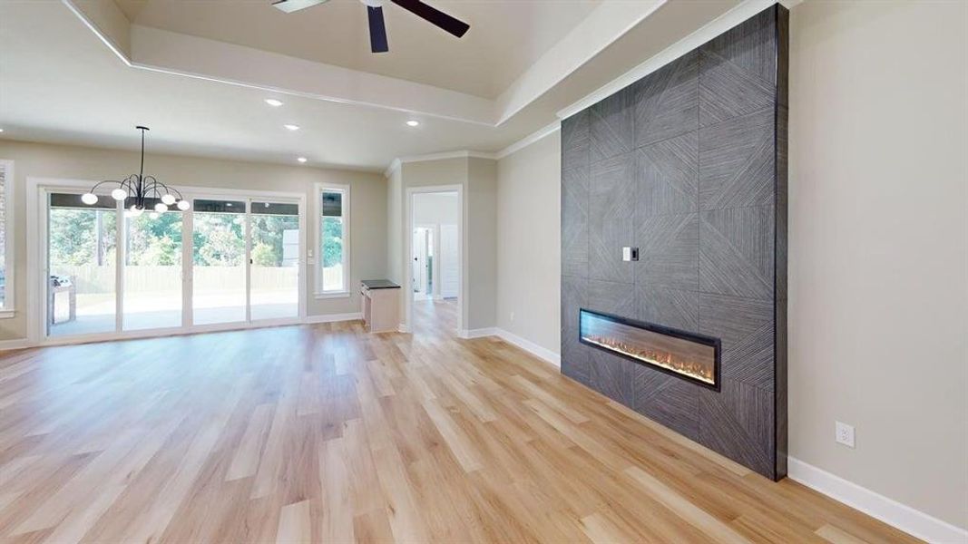Unfurnished living room with a ceiling fan, a tile fireplace, light wood finished floors, recessed lighting, and a chandelier