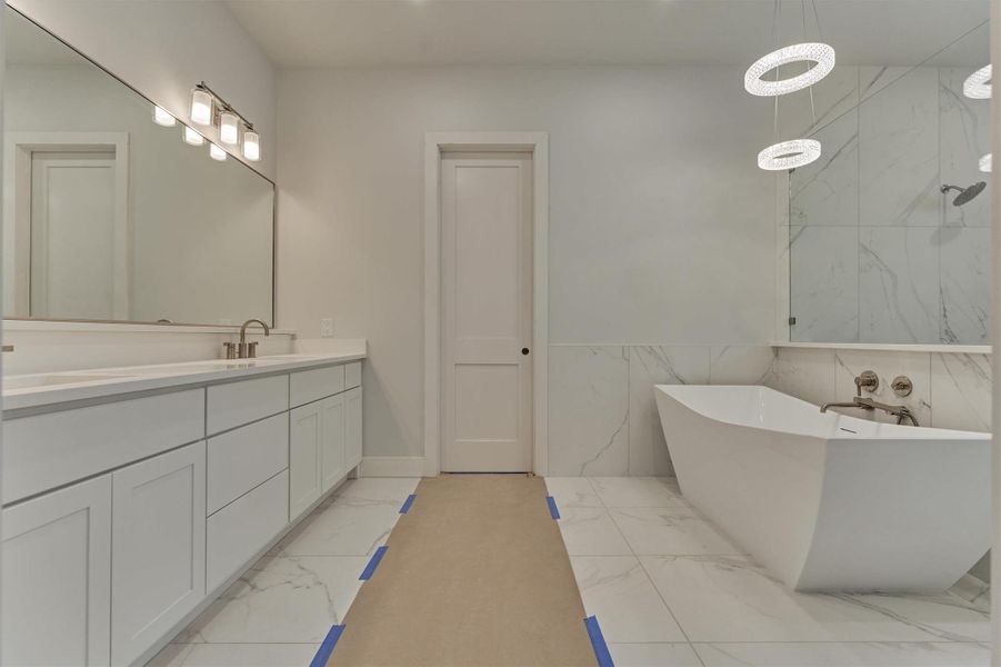 Luxury primary bathroom featuring a sleek double vanity, modern freestanding soaking tub, elegant pendant lighting, and spa-inspired marble-look tile.