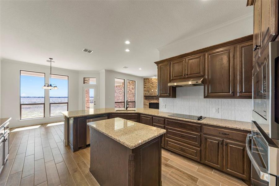 Kitchen with a center island, stainless steel appliances, a peninsula, decorative backsplash, and wood tiled floors Kitchen with a center island, stainless steel appliances, a peninsula, decorative backsplash, and wood tiled floors