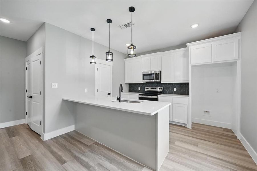 Kitchen with appliances with stainless steel finishes, a sink, a peninsula, white cabinets, and recessed lighting