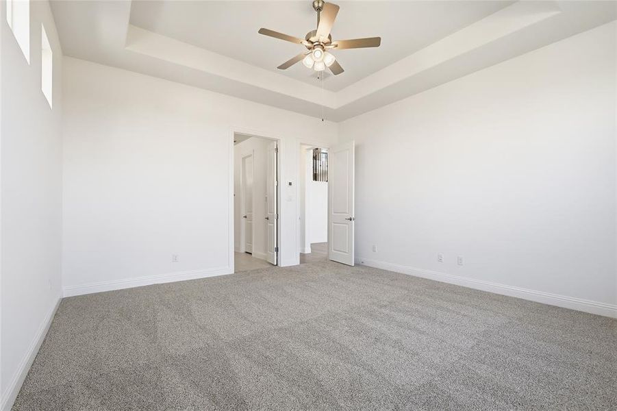 Unfurnished room with a raised ceiling, carpet floors, and ceiling fan Unfurnished room with a raised ceiling, carpet floors, and ceiling fan