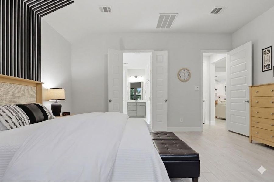 This wide view showcases the primary suite’s consistent plank flooring, window placements, and convenient en suite access.