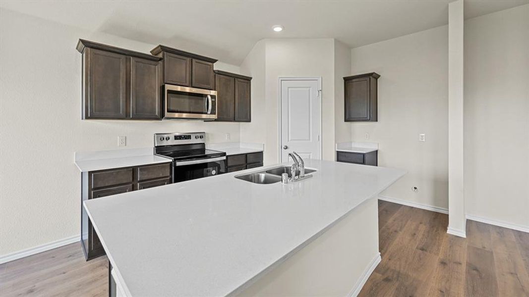Kitchen featuring stainless steel appliances, dark wood finish cabinetry, an island with sink, light stone counters, and dark wood finished floors