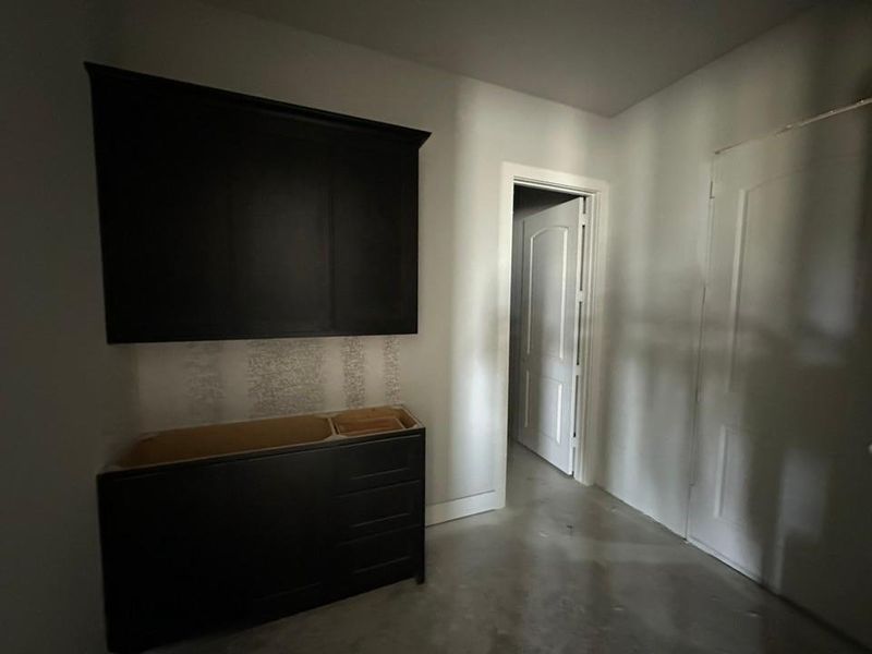 Unfinished space featuring a dark wood-finish vanity base, a coordinating dark wood-finish wall-mounted cabinet, and light-toned patterned wallpaper