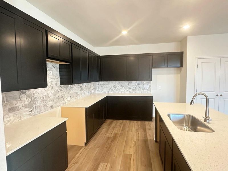 Kitchen featuring decorative backsplash, light stone counters, light wood-style floors, dark cabinets, and recessed lighting Kitchen featuring decorative backsplash, light stone counters, light wood-style floors, dark cabinets, and recessed lighting