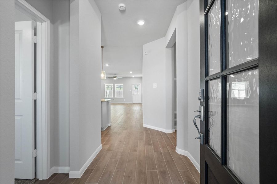 This entryway features a modern, open-concept design. The bright corridor utilizes a neutral color palette, recessed lighting, and wood-look tile flooring to lead the eye toward the home's main living area.