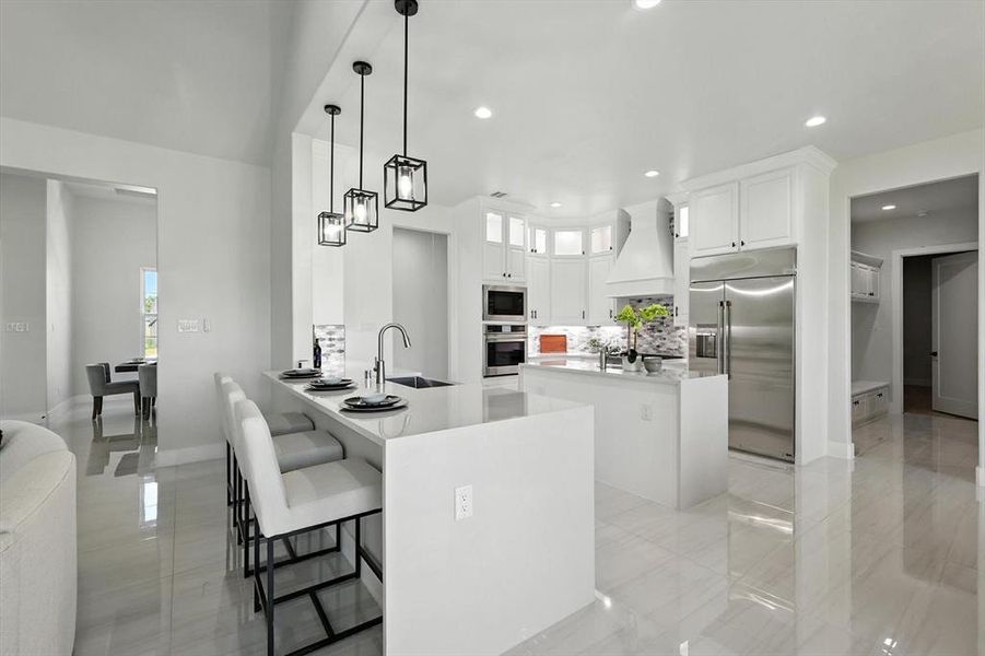 Kitchen featuring built in appliances, a peninsula, custom exhaust hood, a center island, and a kitchen breakfast bar Kitchen featuring built in appliances, a peninsula, custom exhaust hood, a center island, and a kitchen breakfast bar